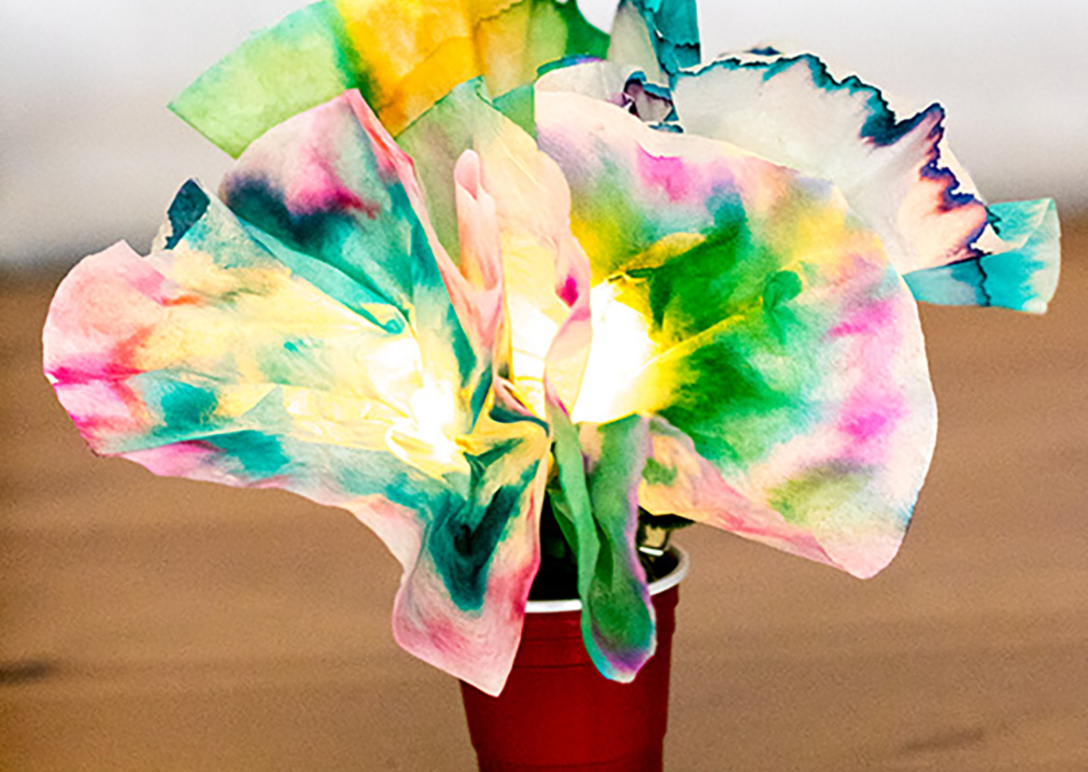 Red solo cup sitting on a wood table, holding tie-dyed paper flowers that are lit up using LED lights