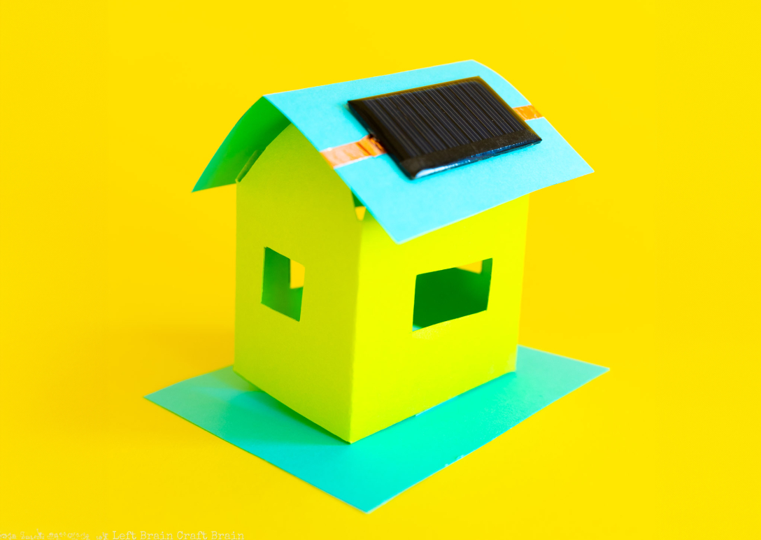Golden yellow background with a small simple house crafted from bright yellow and aqua paper, with a small solar panel attached to the roof.