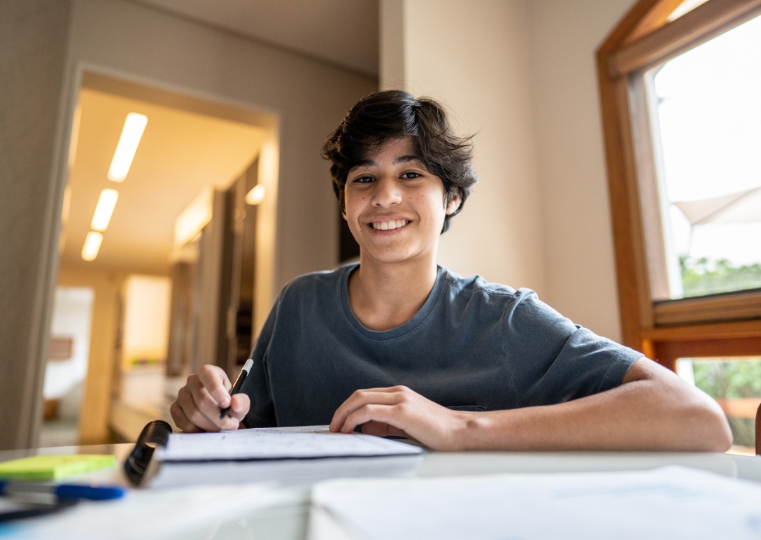 A teenage boy looks up from his notebook to smile at the camera 