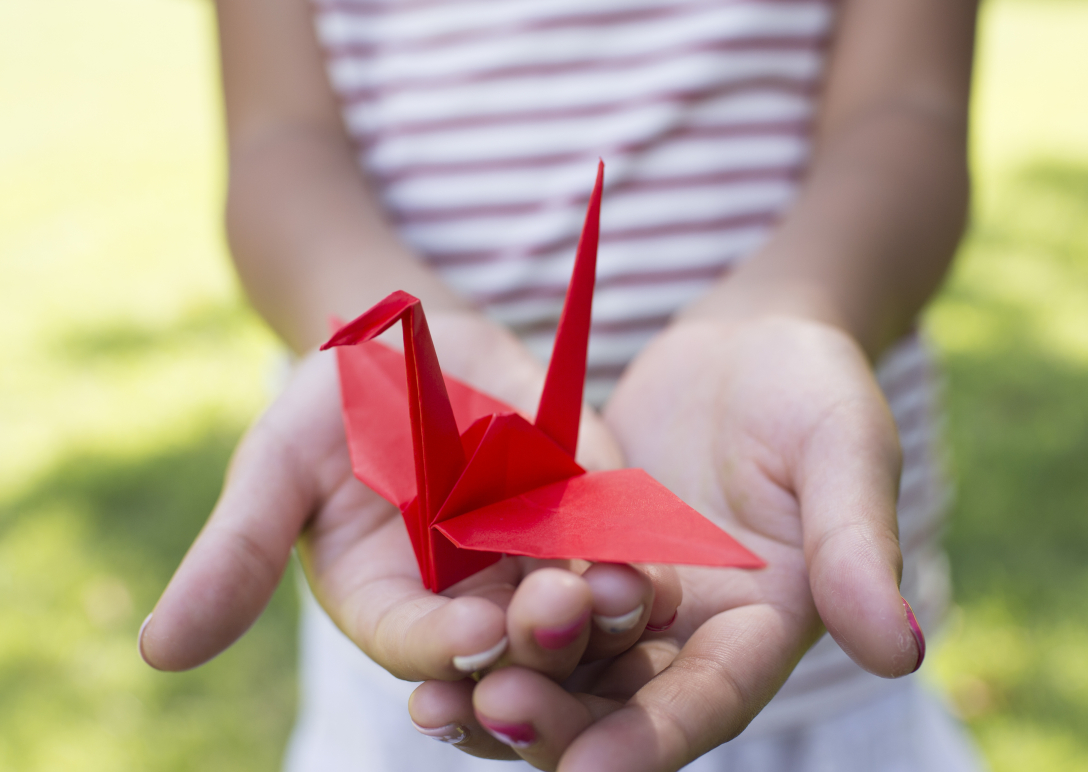 A red origami crane perched in a girl's hands