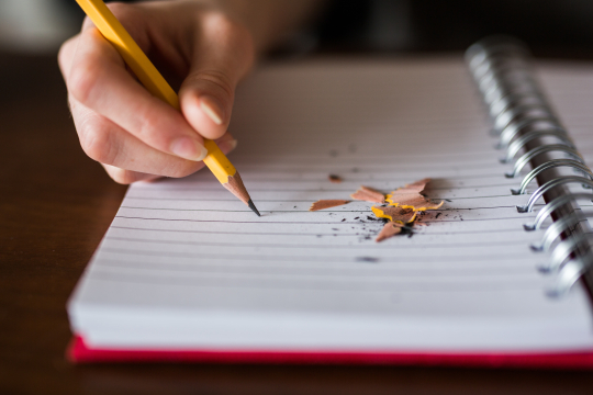 an image of a notebook. Someone is writing on the page and there are pencil shavings next to the pencil.