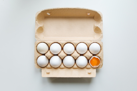 A carton of 10 eggs. The egg in the bottom right corner is cracked open, revealing the yolk.