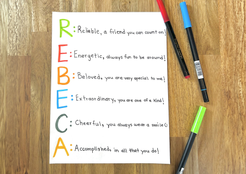 A piece of vertical white paper with the name Rebeca printed on the left in colourful markers