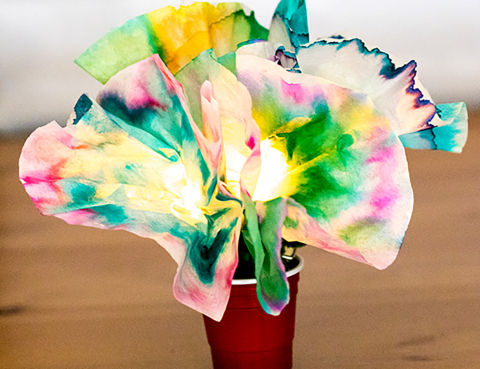 Red solo cup sitting on a wood table, holding tie-dyed paper flowers that are lit up using LED lights