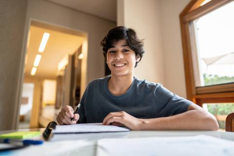 A teenage boy looks up from his notebook to smile at the camera 