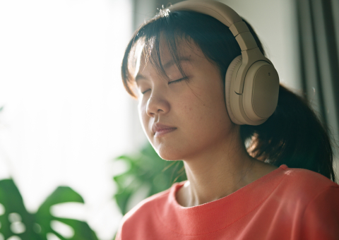a young person with eyes closed, a calm expression and wearing headphones
