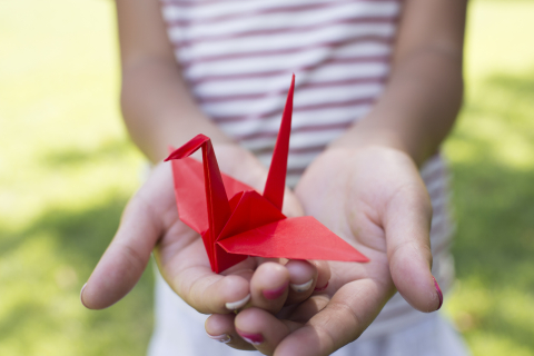 A red origami crane perched in a girl's hands