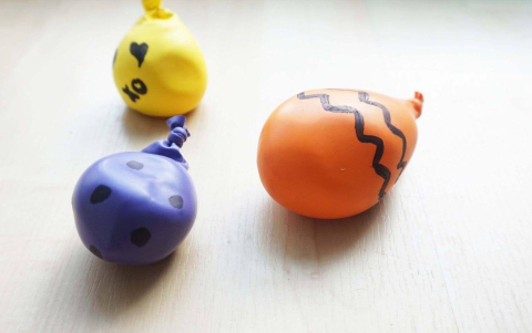 Three decorated, homemade stress balls made from balloons and cornstarch sitting on a table